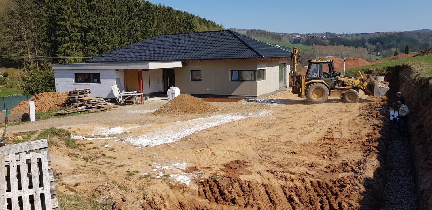 Dokončená střecha černá. Nanesení šedé omítky. Menší okna. Úprava terénu.