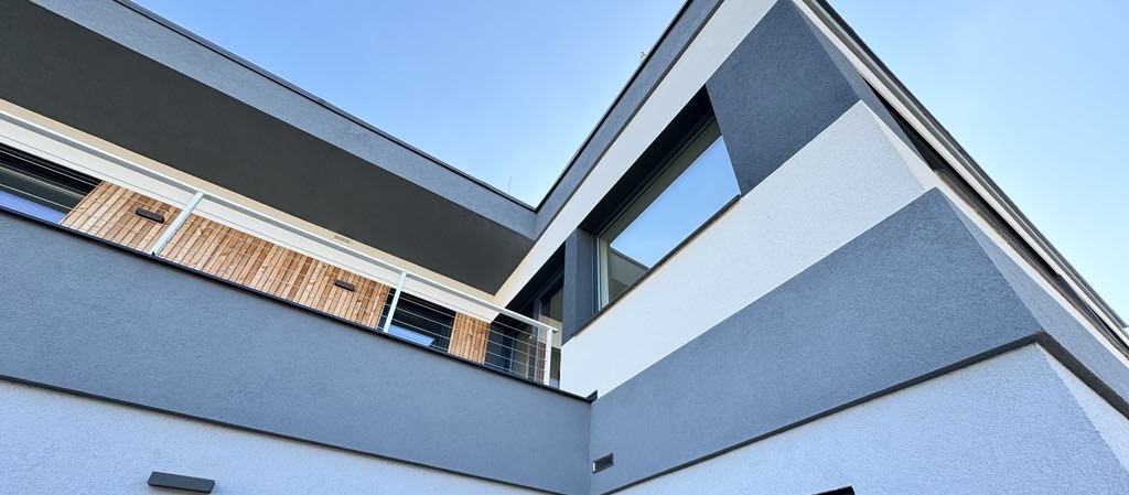 Rekonstrukce rodinného domu Lipí Náchod Dokončená stavba rodinného moderního domu. Šedo-bílá fasáda s dřevěným detailem.