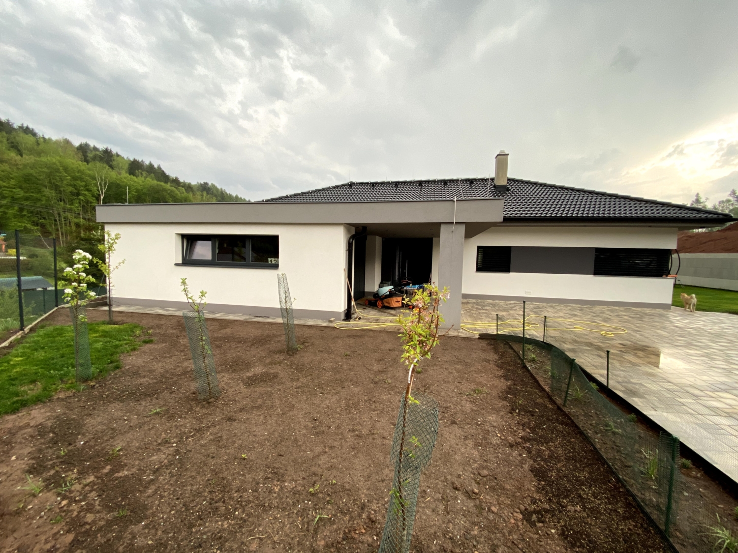 Dokončená výstavba bungalov rodinného domu, Garáž v popředí s oknem, Podpěrný sloup, vchodové dveře, dům s okny. Černá střecha.